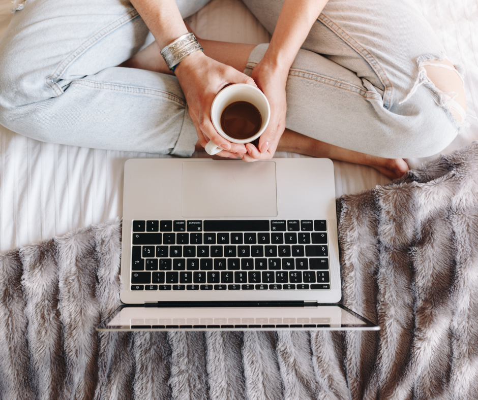Kuvassa tietokone ja henkilö kuvattuna ylhäältä päin. Henkilöllä kahvikuppi käsissä.